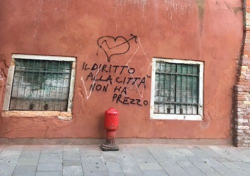 Graffiti against a red wall with a writing reading "il diritto alla città non ha prezzo", in Venice, Italy