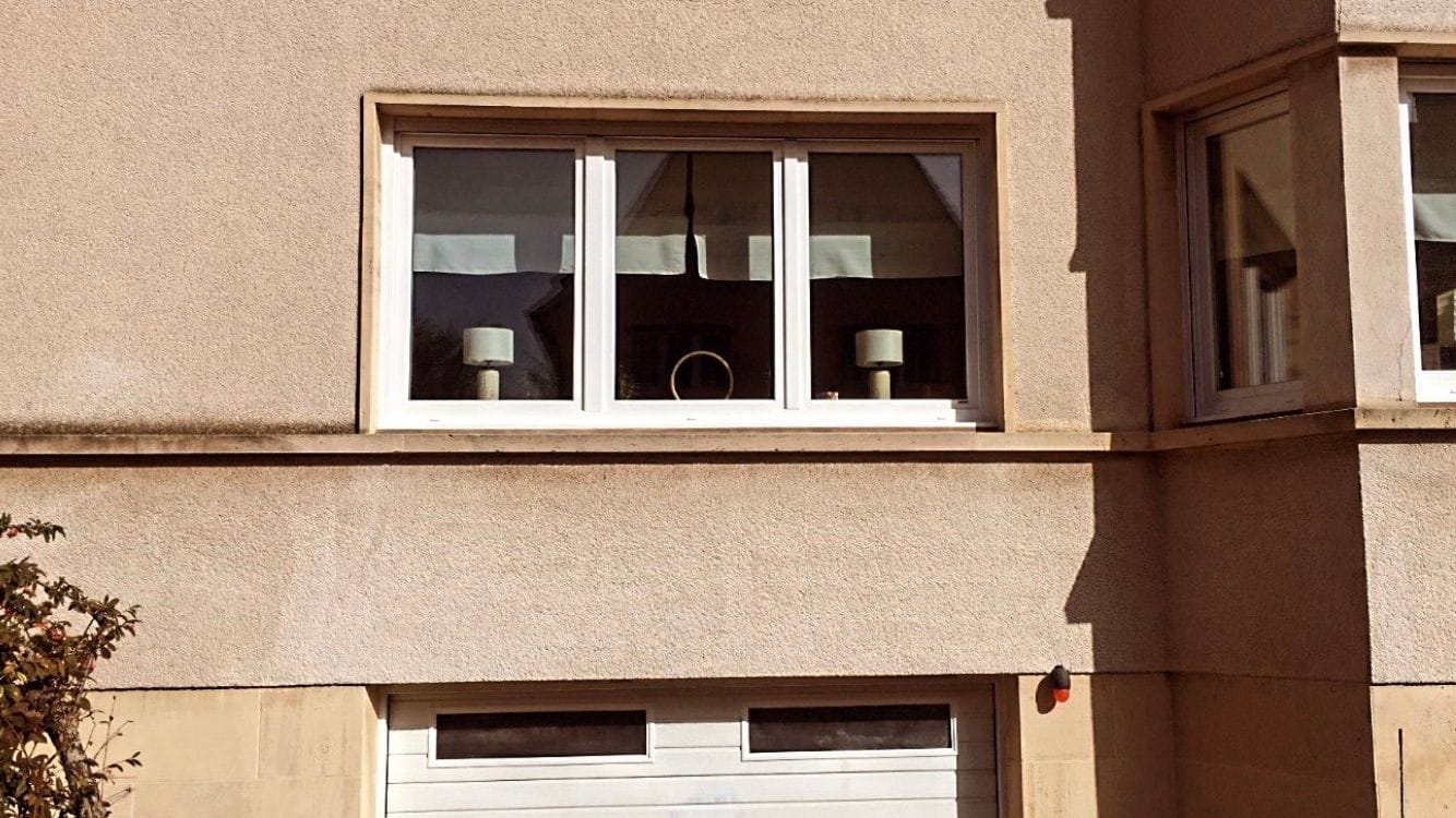 1 window and a white garage door of a yellow house, in Luxembourg.